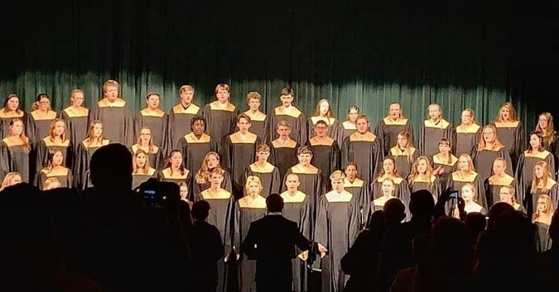 Full choir in black robes singing on stage risers